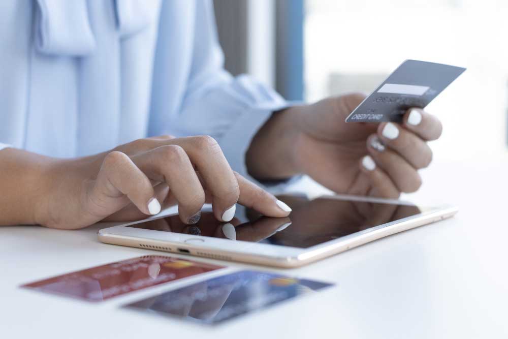 What-Happens-to-My-Credit-Score-After-I-File-Bankruptcy-in-Indiana-4 Hands using a tablet and credit card with extra cards on the table, representing responsible credit use after bankruptcy.