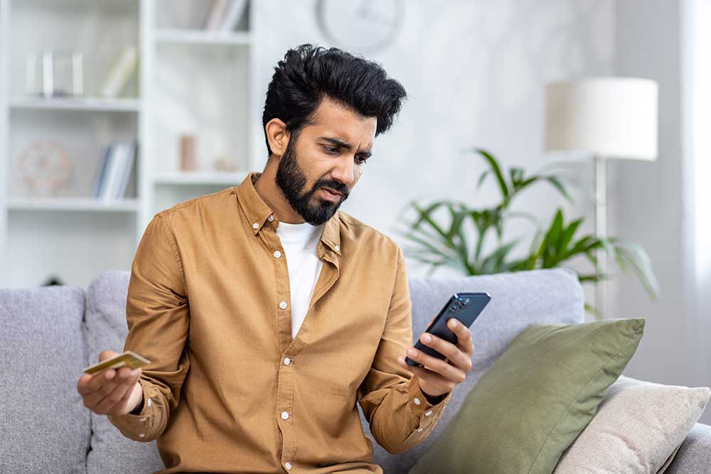 Concerned man holding a credit card and phone while checking debt collection notice, highlighting financial stress.
