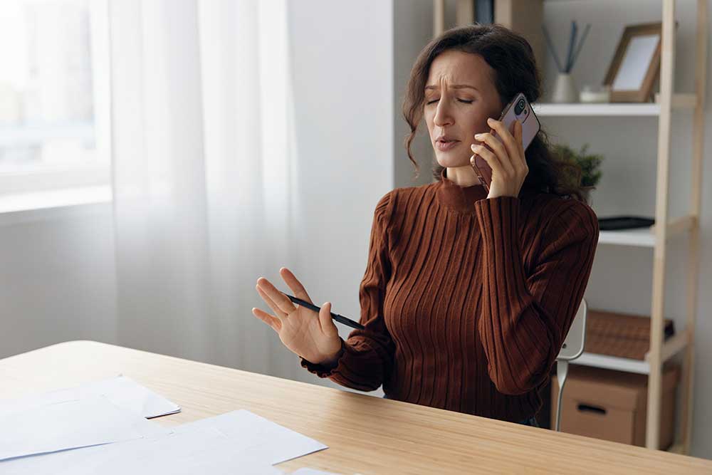 Frustrated woman on phone with debt collector, illustrating unfair collection practices faced by Indiana residents.