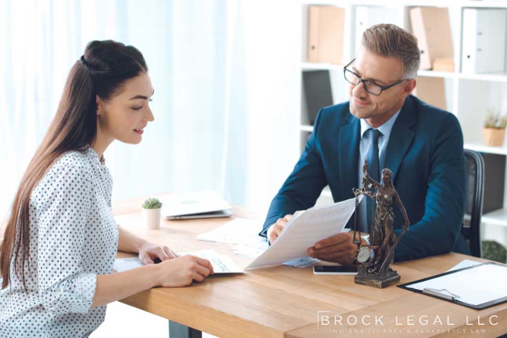 A lawyer from Brock Legal and client sit at a table reviewing legal documents, with a statue of Lady Justice nearby.