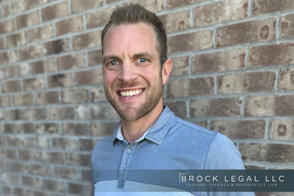 A smiling man in a blue shirt stands against a brick wall. The image represents a trusted Indiana bankruptcy lawyer from Brock Legal, LLC, highlighting their professionalism in providing financial recovery and legal consultation services.| Brock Legal, LLC